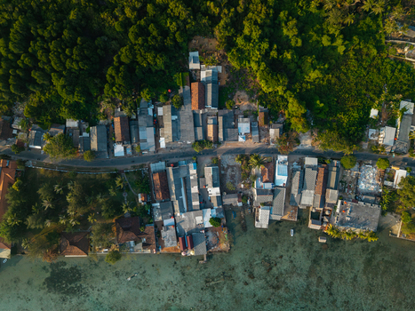 Aerial view of a coastal village with houses nestled between lush tropical trees and the clear turquoise waters of the sea in Karimunjawa Central Java Indonesia. Aerial view of a coastal village with houses nestled between lush tropical trees and the clear turquoise waters of the sea in Karimunjawa Central Java Indonesia.