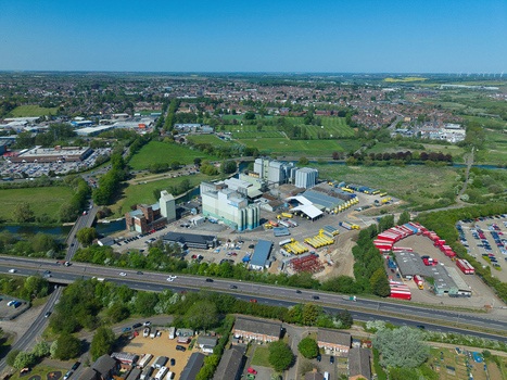 Aerial view of the industrial complex and warehouses with yellow trucks near the A45 road and green fields in Little Irchester England United Kingdom. Aerial view of the industrial complex and warehouses with yellow trucks near the A45 road and green fields in Little Irchester England United Kingdom.