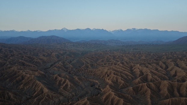 Aerial view of Issyk Kul landscape featuring rugged eroded hills and deep valleys under a clear sky with distant snow capped mountains Issyk Kul Region Kyrgyzstan. Aerial view of Issyk Kul landscape featuring rugged eroded hills and deep valleys under a clear sky with distant snow capped mountains Issyk Kul Region Kyrgyzstan.