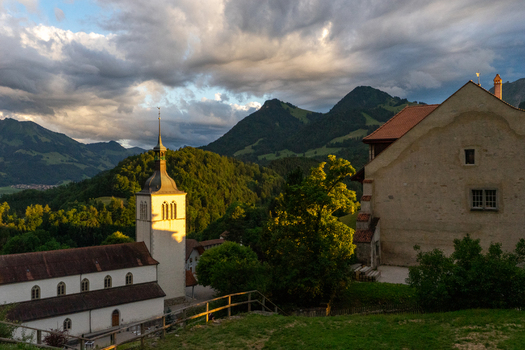 Gruyeres Switzerland 14 May 2026 View of the Church of Saint Theodule and Gruyeres Castle against a backdrop of the Prealps mountains at sunset. Gruyeres Switzerland 14 May 2026 View of the Church of Saint Theodule and Gruyeres Castle against a backdrop of the Prealps mountains at sunset.