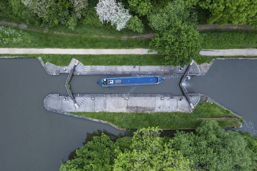 Aerial view of a narrowboat navigating through the historic Hatton Locks surrounded by lush green trees and calm canal water in Hatton England United Kingdom. Aerial view of a narrowboat navigating through the historic Hatton Locks surrounded by lush green trees and calm canal water in Hatton England United Kingdom.