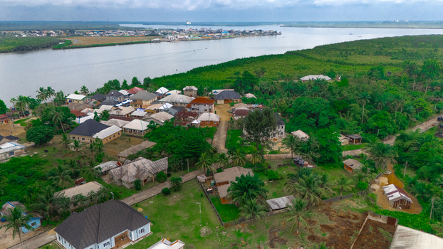Aerial view of a residential village nestled along a riverbank with lush green vegetation scattered houses and palm trees in Minima Rivers Nigeria.