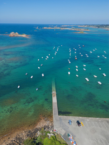 Aerial view of boats anchored in the turquoise waters of Plage de Port Blanc with rocky islands and a concrete pier Penvenan Bretagne France. Aerial view of boats anchored in the turquoise waters of Plage de Port Blanc with rocky islands and a concrete pier Penvenan Bretagne France.