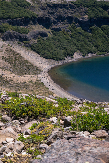 View of the crater lake at Volcan Batea Mahuida featuring steep rocky slopes lush green vegetation and clear blue water in Alumine Neuquen Argentina. View of the crater lake at Volcan Batea Mahuida featuring steep rocky slopes lush green vegetation and clear blue water in Alumine Neuquen Argentina.