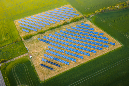 Aerial view of a solar farm with rows of blue photovoltaic panels surrounded by lush green agricultural fields during golden hour in Chvalkovice Hradec Kralove Region Czechia.