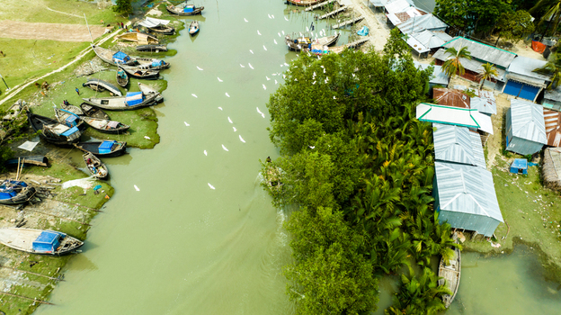 Aerial view of Patharghata river with wooden fishing boats moored along muddy banks surrounded by mangroves and houses in Patharghata Barisal Division Bangladesh. Aerial view of Patharghata river with wooden fishing boats moored along muddy banks surrounded by mangroves and houses in Patharghata Barisal Division Bangladesh.