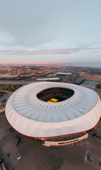 Aerial view of Riyadh Air Metropolitano Stadium with its distinctive circular roof and illuminated pitch set against the urban landscape of Madrid Comunidad de Madrid Spain.