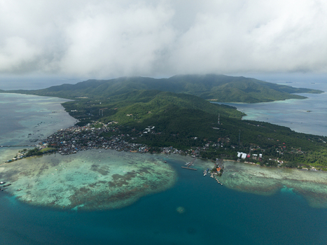 Aerial view of a lush island with turquoise waters lapping against the shore houses dotting the coastline Karimunjawa Central Java Indonesia. Aerial view of a lush island with turquoise waters lapping against the shore houses dotting the coastline Karimunjawa Central Java Indonesia.