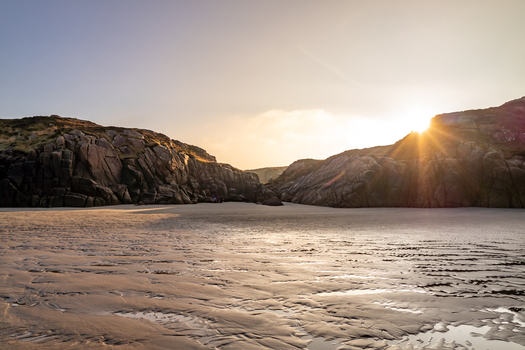 View of the sandy beach framed by rugged rocky cliffs under a warm golden sunset light Cloughglass County Donegal Ireland. View of the sandy beach framed by rugged rocky cliffs under a warm golden sunset light Cloughglass County Donegal Ireland.