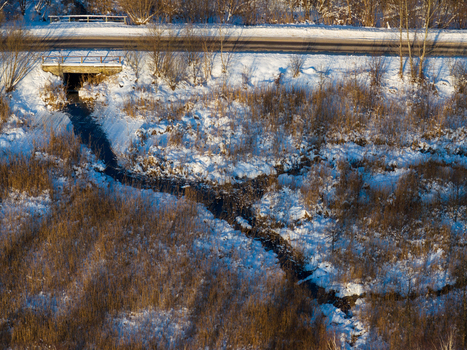 Aerial view of a small stream flowing from a culvert under a road through snow covered reeds and winter vegetation Lithuania. Aerial view of a small stream flowing from a culvert under a road through snow covered reeds and winter vegetation Lithuania.
