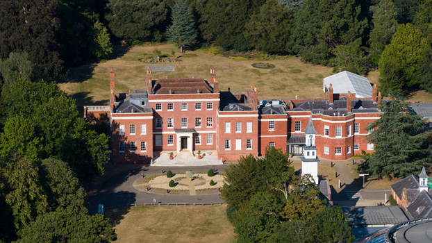 Aerial view of Hinxton Hall at the Wellcome Genome Campus featuring the historic red brick mansion surrounded by lush green trees and manicured grounds in Hinxton England United Kingdom. Aerial view of Hinxton Hall at the Wellcome Genome Campus featuring the historic red brick mansion surrounded by lush green trees and manicured grounds in Hinxton England United Kingdom.