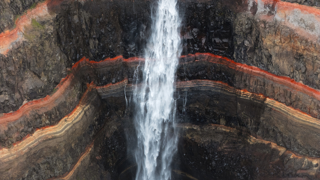 Aerial view of the Hengifoss waterfall cascading down the cliff s basalt layered rock face with striking red clay bands Hengifoss Iceland.