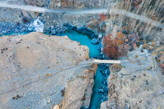 Aerial view of a narrow rustic bridge spanning the turquoise river in the rugged Chapursan Valley Hunza Nagar Gilgit Pakistan. Aerial view of a narrow rustic bridge spanning the turquoise river in the rugged Chapursan Valley Hunza Nagar Gilgit Pakistan.