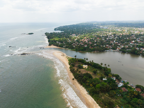 Aerial view of the Nilwala River mouth meeting the Indian Ocean with sandy beaches lush palm trees and the coastal cityscape of Matara Southern Province Sri Lanka. Aerial view of the Nilwala River mouth meeting the Indian Ocean with sandy beaches lush palm trees and the coastal cityscape of Matara Southern Province Sri Lanka.