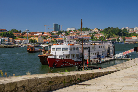Porto Portugal 13 July 2021 View of boats docked on the Douro River under a bright blue sky with the city s terracotta rooftops rising in the background. Porto Portugal 13 July 2021 View of boats docked on the Douro River under a bright blue sky with the city s terracotta rooftops rising in the background.