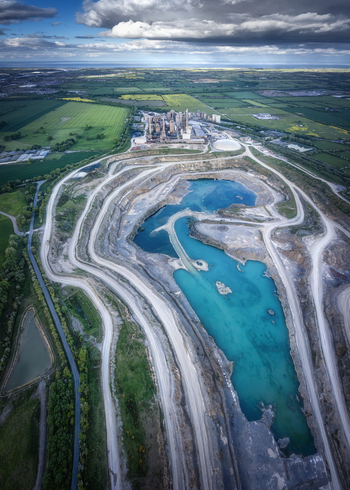 Aerial view of the Irish Cement Ltd plant and limestone quarry with turquoise water pools and winding roads surrounded by green fields Drogheda County Louth Ireland.
