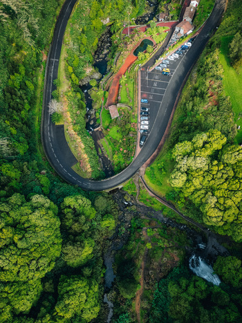 Aerial view of a winding road cutting through lush green vegetation with cars parked near red roofed buildings Achada Açores Portugal. Aerial view of a winding road cutting through lush green vegetation with cars parked near red roofed buildings Achada Açores Portugal.