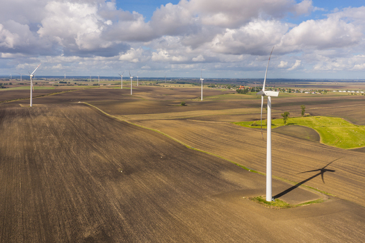 Aerial view of wind turbines standing in a vast agricultural field with brown soil under a blue sky with white clouds in Pomeranian Voivodeshi Poland. Aerial view of wind turbines standing in a vast agricultural field with brown soil under a blue sky with white clouds in Pomeranian Voivodeshi Poland.