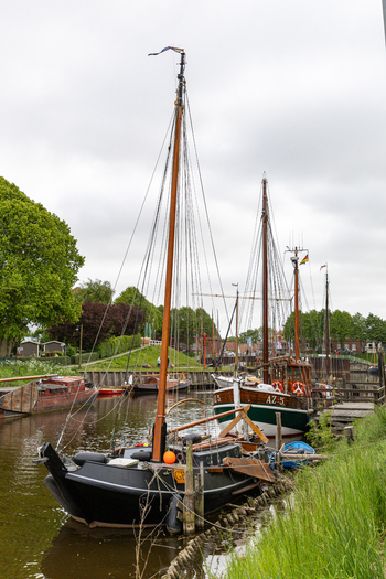View of Hafen Harlesiel with traditional wooden sailing boats moored along the canal bank with lush green trees and an overcast sky Wittmund Lower Saxony Germany. View of Hafen Harlesiel with traditional wooden sailing boats moored along the canal bank with lush green trees and an overcast sky Wittmund Lower Saxony Germany.