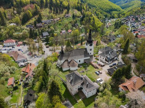 Aerial view of the Church of the Transfiguration of the Lord and historic houses nestled in the lush green hills of the mining village Spania Dolina Banska Bystrica Regio Slovakia.