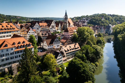 Aerial view of the historic old town with red tiled roofs the Stiftskirche tower and the Neckar river lined with green trees in Tubingen Baden Wurttemberg Germany. Aerial view of the historic old town with red tiled roofs the Stiftskirche tower and the Neckar river lined with green trees in Tubingen Baden Wurttemberg Germany.