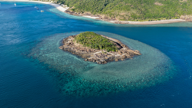 Aerial view of Haslewood Island surrounded by turquoise coral reefs and deep blue ocean waters in Whitsundays Queensland Australia. Aerial view of Haslewood Island surrounded by turquoise coral reefs and deep blue ocean waters in Whitsundays Queensland Australia.