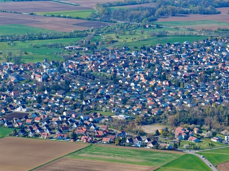 Aerial view of rooftops nestled tightly together a mosaic of red and brown against the green and gold of surrounding fields Sausheim Grand Est France.
