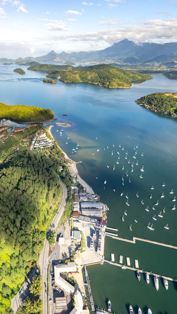 Aerial view of a marina with numerous sailboats anchored in the calm blue bay surrounded by lush green hills and coastal mountains in Angra dos Reis Rio de Janeiro Brazil.