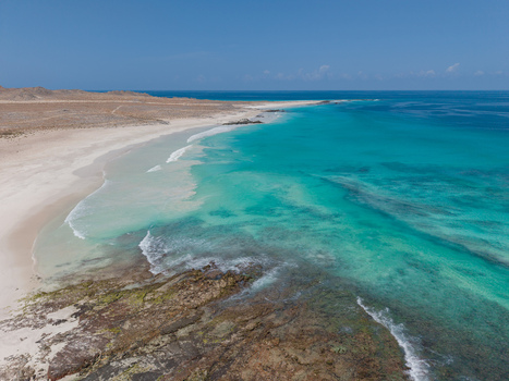 Aerial view of the serene meeting of white sands and turquoise waters framed by the rugged coastline under a vast blue sky Erissiel Socotra Yemen.