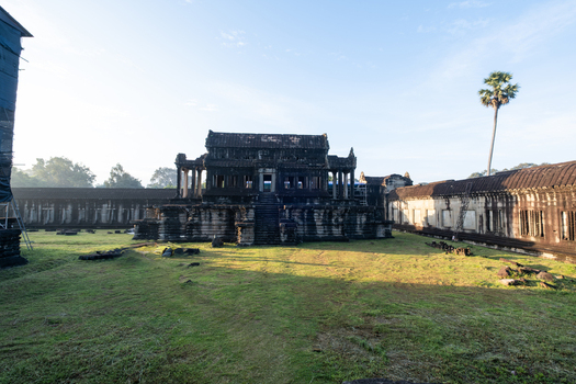 View of the ancient stone architecture and central sanctuary of Angkor Wat temple complex with a grassy courtyard and palm tree in Krong Siem Reap Siem Reap Province Cambodia.