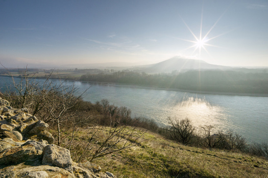 View of the Danube river from the historic Devin Castle grounds with a bright sun starburst over hazy hills and stone walls in Bratislava IV Bratislava Region Slovakia. View of the Danube river from the historic Devin Castle grounds with a bright sun starburst over hazy hills and stone walls in Bratislava IV Bratislava Region Slovakia.