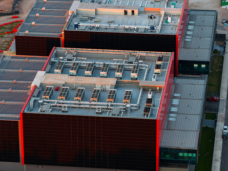 Aerial view of a modern datacenter featuring industrial HVAC units on the rooftop and a distinctive red and black facade in Settecamini Lazio Italy.