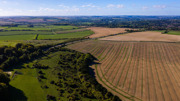 Aerial view of the rolling landscape of National Trust Pepperbox Hill with harvested fields lush green trees and a road winding through the countryside in Salisbury England United Kingdom. Aerial view of the rolling landscape of National Trust Pepperbox Hill with harvested fields lush green trees and a road winding through the countryside in Salisbury England United Kingdom.