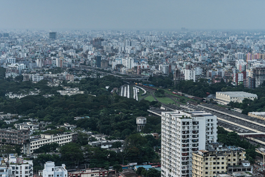 Dhaka Dhaka Division Bangladesh 30 June 2025 Aerial view of the dense urban landscape of Dhaka featuring a railway yard lush green trees and high rise residential buildings under a hazy sky.