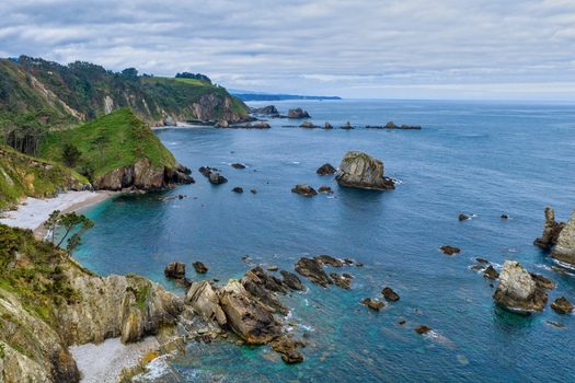 Aerial view of Silence Beach Viewpoint with rugged cliffs turquoise water and rocky formations under a cloudy sky in Cudillero Asturias Spain.