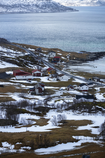 View of colorful wooden houses along a coastal road by a fjord with snow covered patches Kvaloya Troms Norway. View of colorful wooden houses along a coastal road by a fjord with snow covered patches Kvaloya Troms Norway.