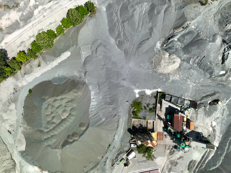 Aerial view of large grey gravel piles and industrial processing machinery at a quarry site with green trees along the perimeter in Caprie Piedmont Italy. Aerial view of large grey gravel piles and industrial processing machinery at a quarry site with green trees along the perimeter in Caprie Piedmont Italy.