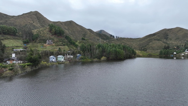 Aerial view of Corani Lake with small houses nestled along the shore surrounded by pine trees and rolling hills under an overcast sky in Chapare Cochabamba Department Bolivia. Aerial view of Corani Lake with small houses nestled along the shore surrounded by pine trees and rolling hills under an overcast sky in Chapare Cochabamba Department Bolivia.