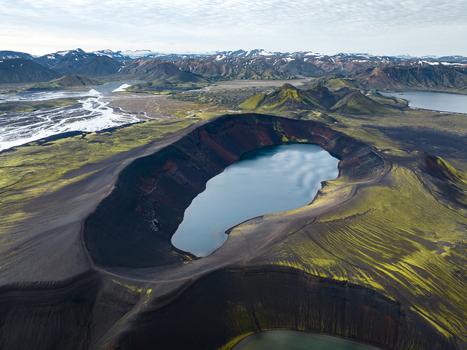 Aerial view of the striking contrast between the dark volcanic earth vibrant green moss and the serene blue lake within the crater Highlands Iceland.