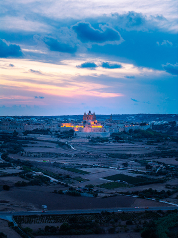 Aerial view of the historic fortified city of Mdina illuminated at twilight featuring the cathedral and ancient walls surrounded by rural fields in Mdina Western Region Malta. Aerial view of the historic fortified city of Mdina illuminated at twilight featuring the cathedral and ancient walls surrounded by rural fields in Mdina Western Region Malta.