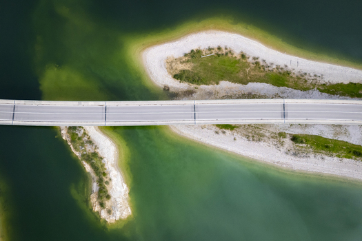 Aerial view of a bridge slicing through the emerald waters connecting sandy shores touched by verdant patches Sylvensteinspeicher Bayern Germany. Aerial view of a bridge slicing through the emerald waters connecting sandy shores touched by verdant patches Sylvensteinspeicher Bayern Germany.