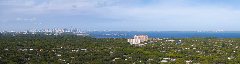 Aerial view of the lush green canopy of residential neighborhoods with the distant city skyline and Biscayne Bay under a clear blue sky Coral Gables Florida United States.