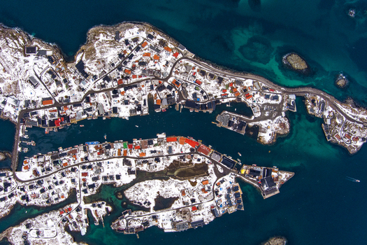 Aerial view of the Lofoten archipelago in winter featuring snow covered coastal villages with colorful houses winding roads and turquoise waters Nordland Norway.