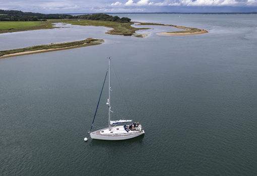 Aerial view of a sailboat anchored in the calm waters of Newtown Creek surrounded by coastal marshes and green fields in the Isle Of Wight United Kingdom.