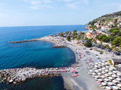 Aerial view of the coastline with stone breakwaters sandy beach with umbrellas and palm trees in San Lorenzo Liguria Italy.