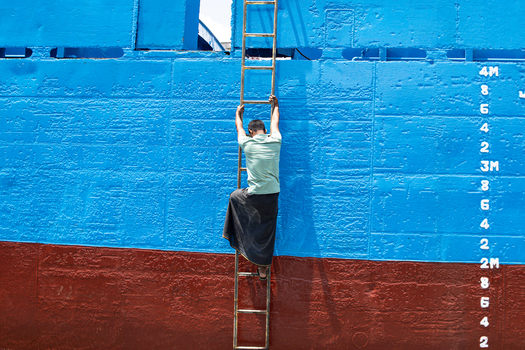Keraniganj Bangladesh 04 September 2024 View of a worker climbing a metal ladder against the vibrant blue and red hull of a ship at Shipyard Dhaka.