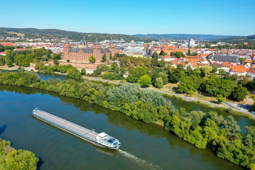Aerial view of Schloss Johannisburg and a cargo barge on the Main river surrounded by green trees and the city skyline in Aschaffenburg Bayern Germany. Aerial view of Schloss Johannisburg and a cargo barge on the Main river surrounded by green trees and the city skyline in Aschaffenburg Bayern Germany.