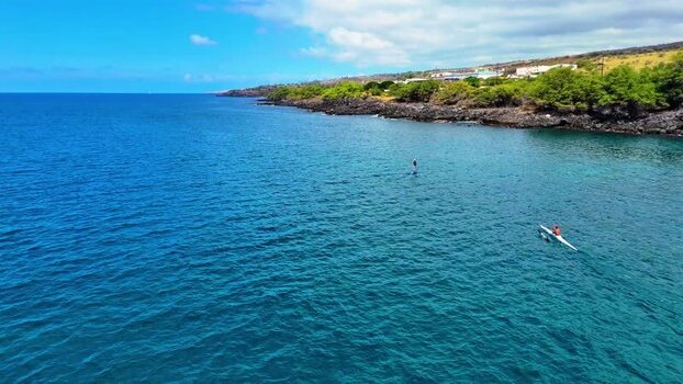 Aerial view of a man on an electric hydrofoil and a one man outrigger canoe on the blue water of Kawaihae United States. Aerial view of a man on an electric hydrofoil and a one man outrigger canoe on the blue water of Kawaihae United States.