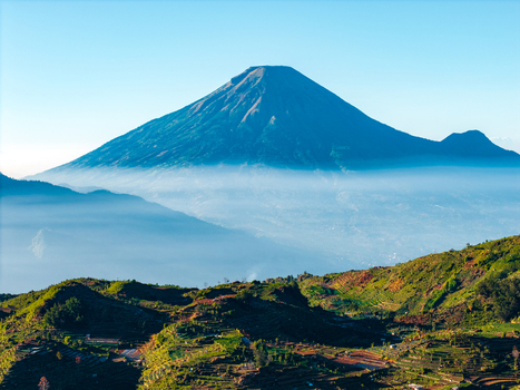 Aerial view of Mount Sindoro rising above terraced agricultural fields and a layer of morning mist in the Dieng Plateau Kecamatan Kejajar Jawa Tengah Indonesia. Aerial view of Mount Sindoro rising above terraced agricultural fields and a layer of morning mist in the Dieng Plateau Kecamatan Kejajar Jawa Tengah Indonesia.