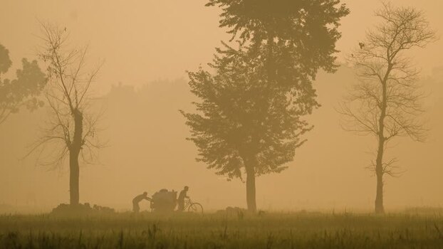 View of people pushing a cart through a misty field Bangladesh.